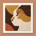 Punch needle wall art of an abstract cat face in golden mustard, espresso brown, and terracotta geometric blocks