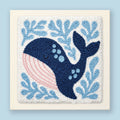 Punch needle kit showing a smiling navy blue whale with a pink belly among soft blue sea botanicals on cream