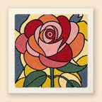 Punch needle kit with a large blooming rose in dusty rose, burnt orange, and deep red on a slate blue background