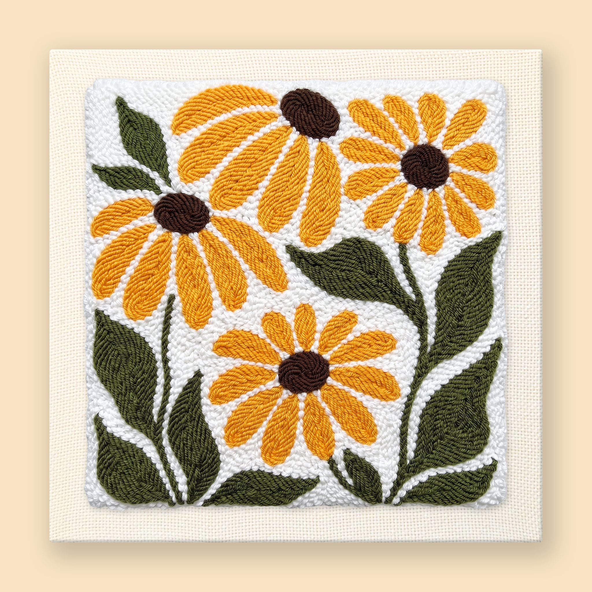 Punch needle wall art of four golden black-eyed Susan flowers with olive green leaves on a cream background