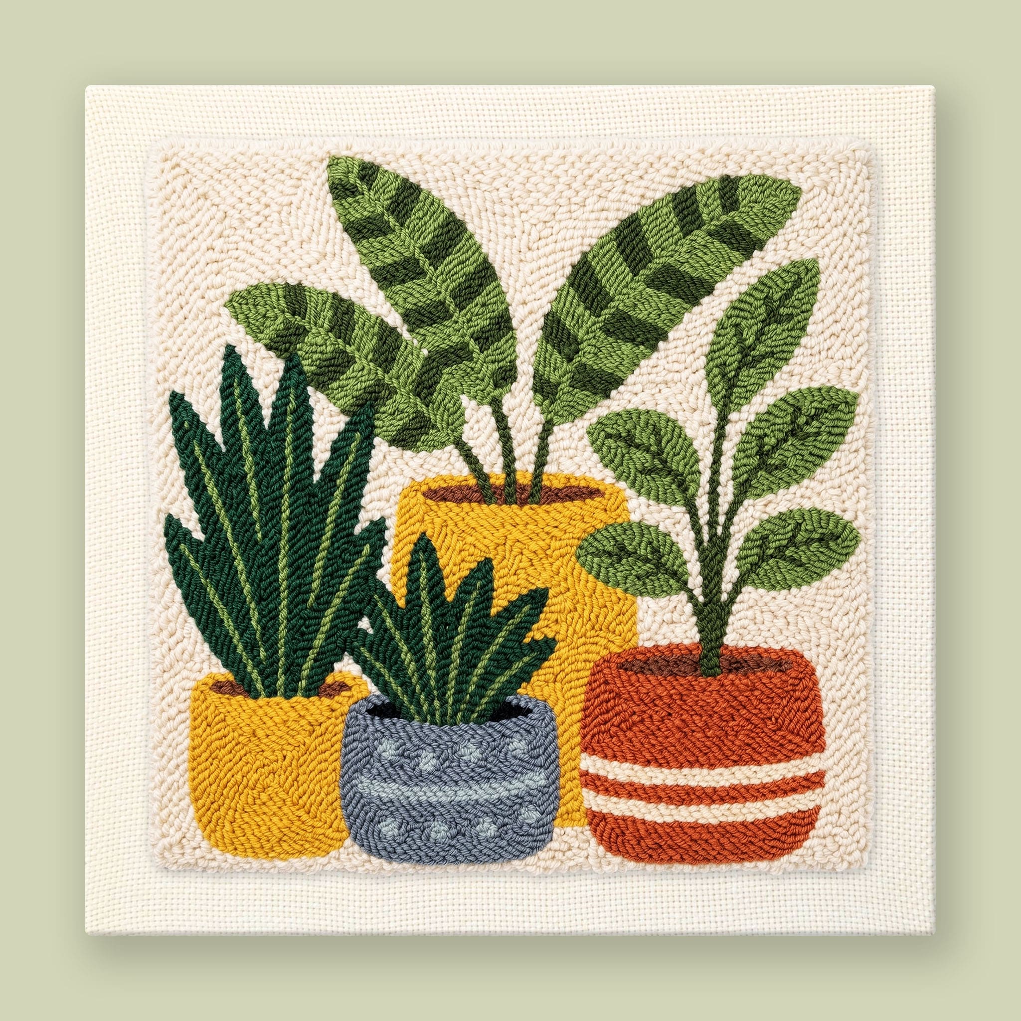 Punch needle wall art of three houseplants in mustard, terracotta, and slate blue pots on a cream background