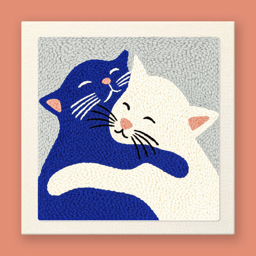 Heartwarming punch needle art of a navy blue cat and white cat hugging with sweet smiling faces on gray background