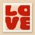 Modern punch needle wall art spelling LOVE in bold graphic letters with red and cream colors